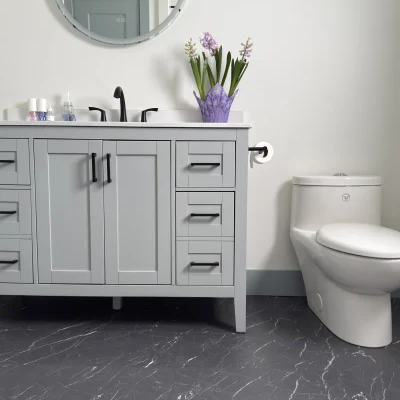 A contemporary bathroom featuring a light grey vanity with black hardware, a round framed mirror, a white toilet, and dark grey marble-style flooring.