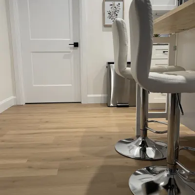 Light wood plank flooring installed in a home, featuring a white interior door with black hardware and a kitchen island with white bar stools.