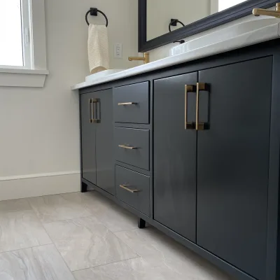 A custom dark blue bathroom vanity with gold hardware and a white countertop, paired with light grey tile flooring and a black framed mirror.
